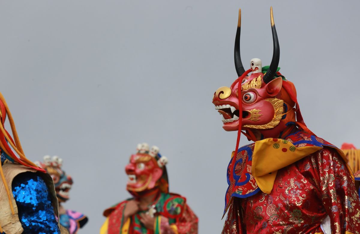 Masked dancers in red silk costume at a Bhutanese tshechu